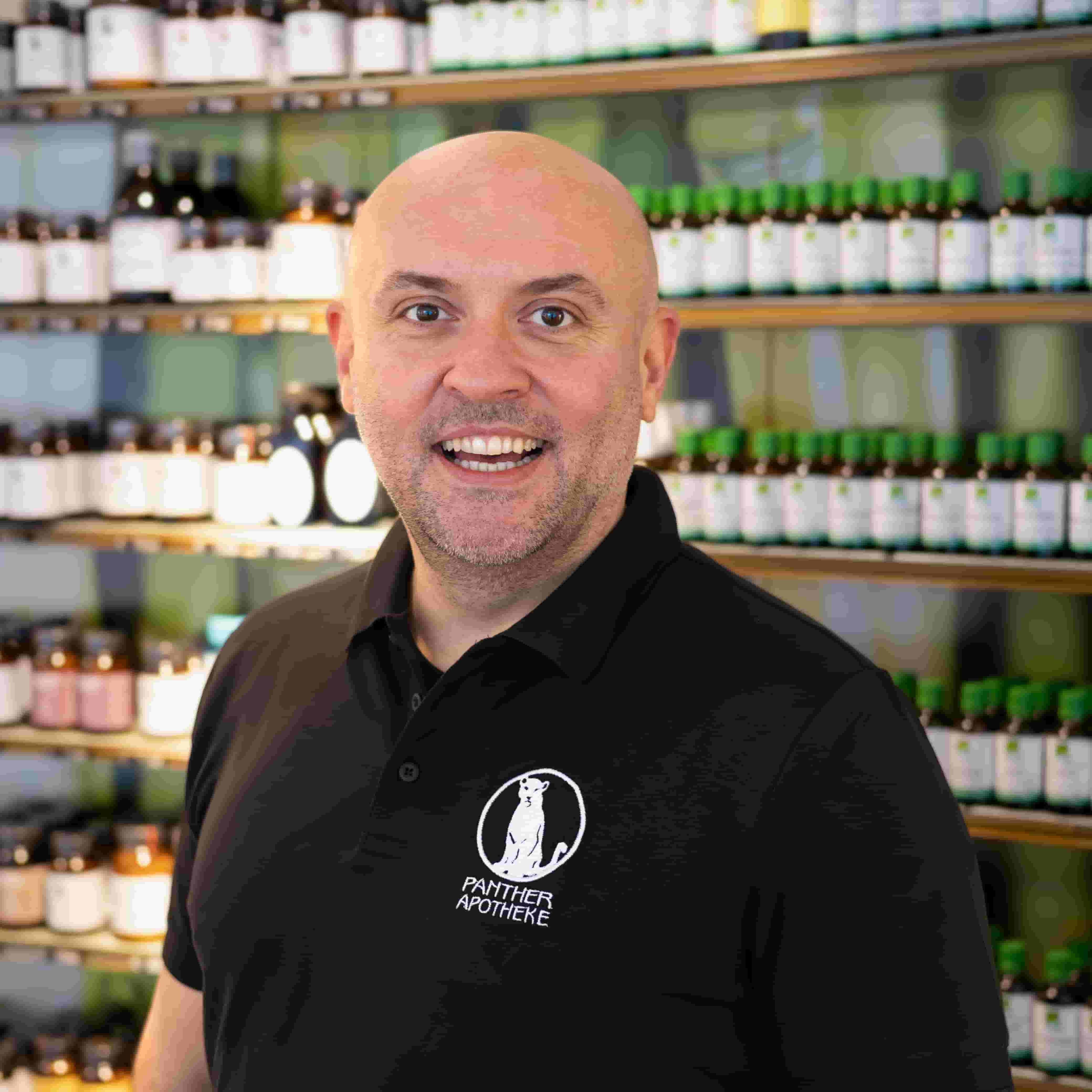 Porträt von Mag. pharm. Pece Petrovski, stehend vor einem Produktregal.